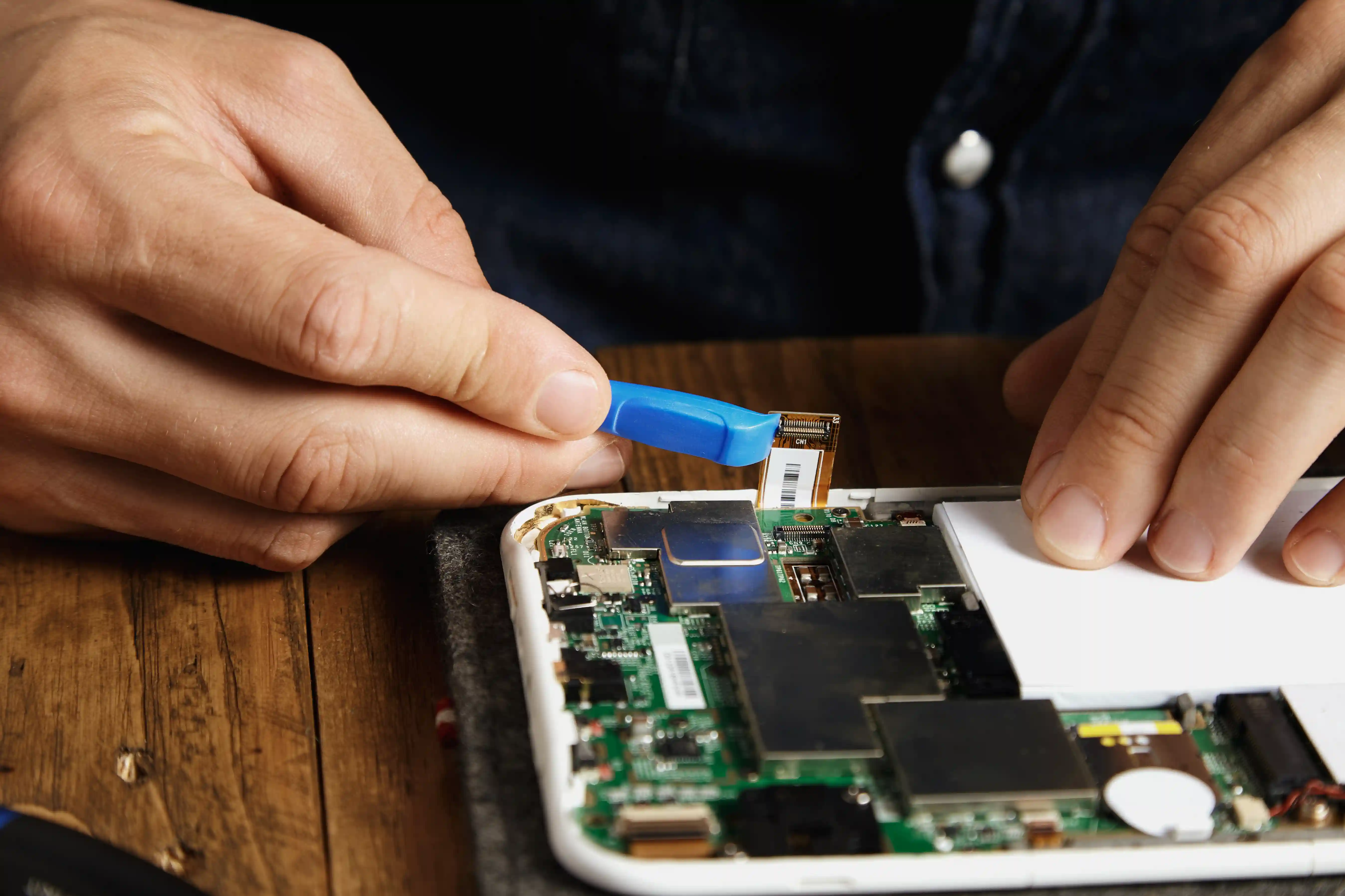 Technician repairing an open smartphone motherboard and connector with a precision tool