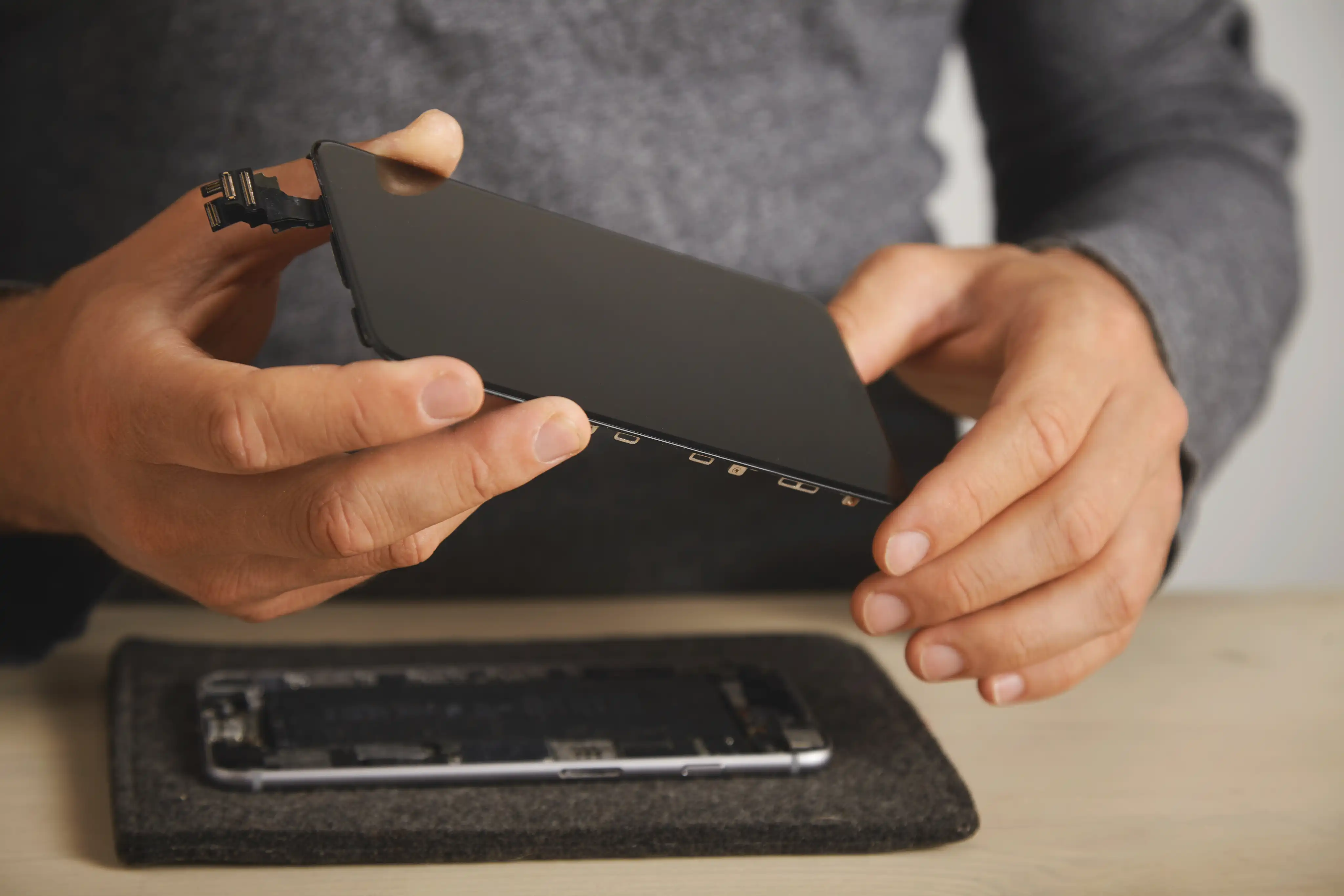 Technician fitting a replacement screen onto a smartphone during a phone repair